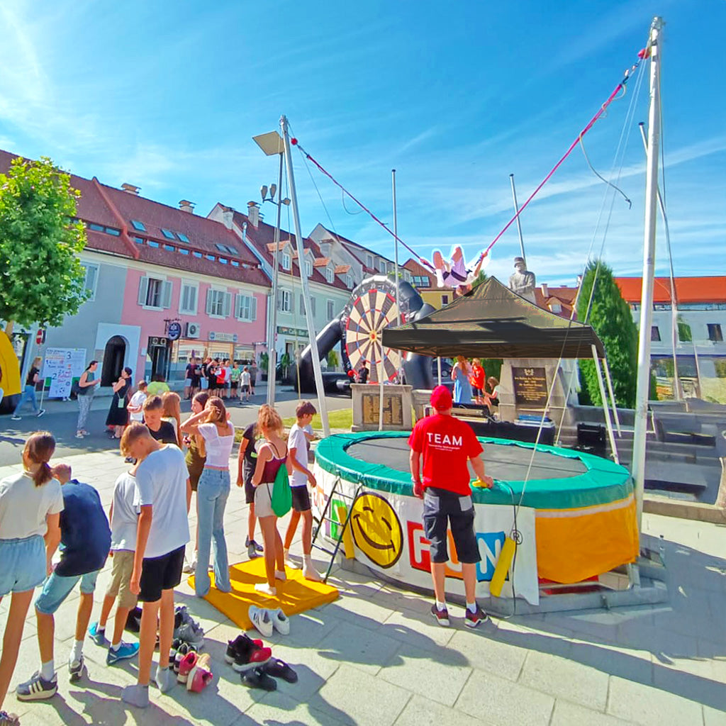 Ein Bungee Trampolin von Happy Fun zum mieten, viele Kinder und Teenager in einer Warteschlange wollen hüpfen.