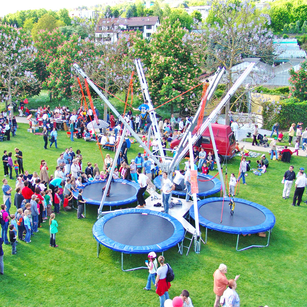 Kinder, Jugendliche und Erwachsene auf einem Event die bei einem 4er Bungee Trampolin anstehen und Kinder die bereits springen.