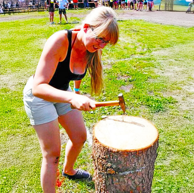 Dame mit langen blonden Haaren beim Baumstammnageln im Freien