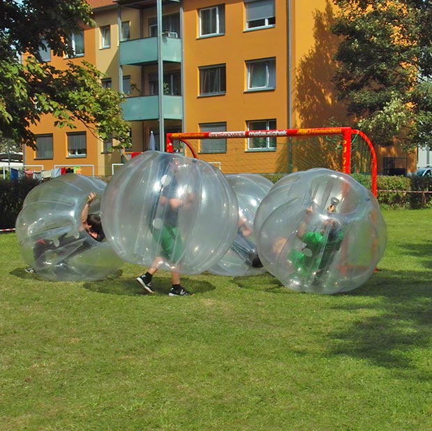 Kinder in Aufblasbaren Bubble Baellen vor einem roten Tor auf einer Wiese.