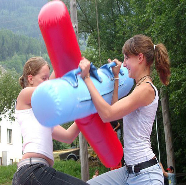 Zwei Maedchen die Spass bei einem Gladiatoren Wettkampf mit zwei gepolsterten Staeben haben.