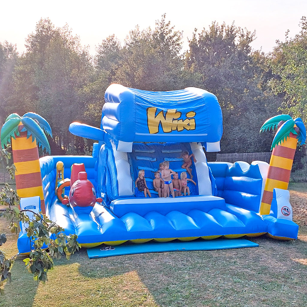 Aufblasbare Maulrutsche - Wal zum mieten mit Palmen und Kinder die im Maul des Wals sitzen.