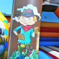 Freundlicher Cowboy mit Hut auf einer Saeule einer aufblasbaren Huepfburg.