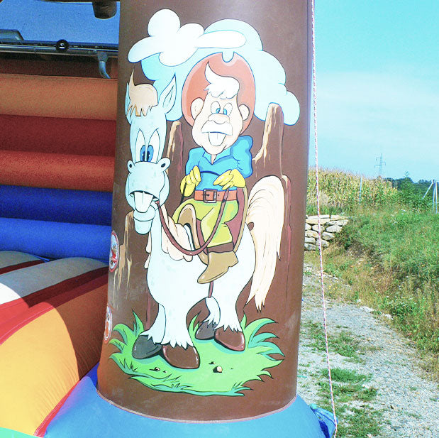 Ein aufgemalter Cowboy, der auf einem weissen Pferd sitzt auf einer Saeule einer aufblasbaren Huepfburg