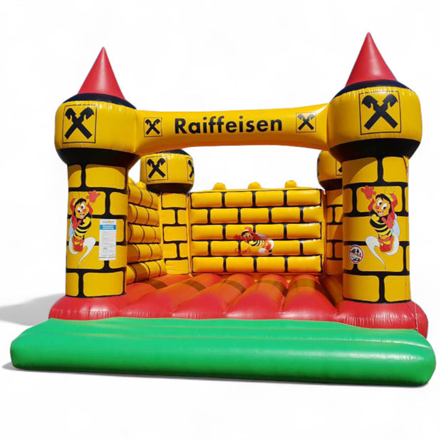 Gelbe Hüpfburg im Burgdesign mit Sumsi-Motiven – Sonderanfertigung für Raiffeisenbank mit individuellem Branding