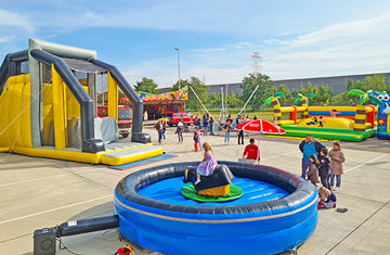 Buntes Outdoor-Event auf einem großen Platz mit mehreren Hüpfburgen, einer aufblasbaren Riesenrutsche, einem mechanischen Rodeo-Bullen und zahlreichen Besuchern, darunter viele Kinder und Familien.
