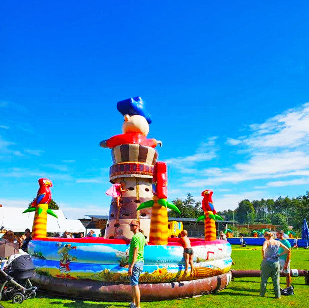 Kinder und Erwachsene auf einem Fest mit einem Pirat Kletterturm auf einer Wiese