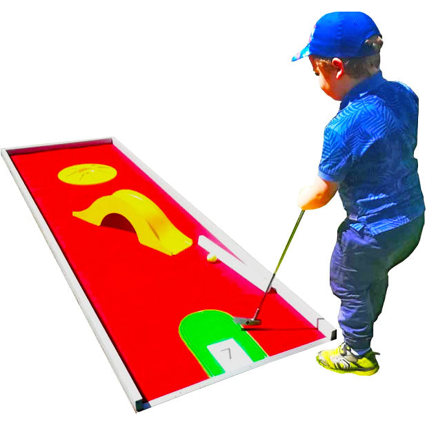 Kleiner Junge mit einer blauen Kappe auf dem Kopf und einem Minigolf Schlaeger in der Hand bei einer Minigolfbahn.