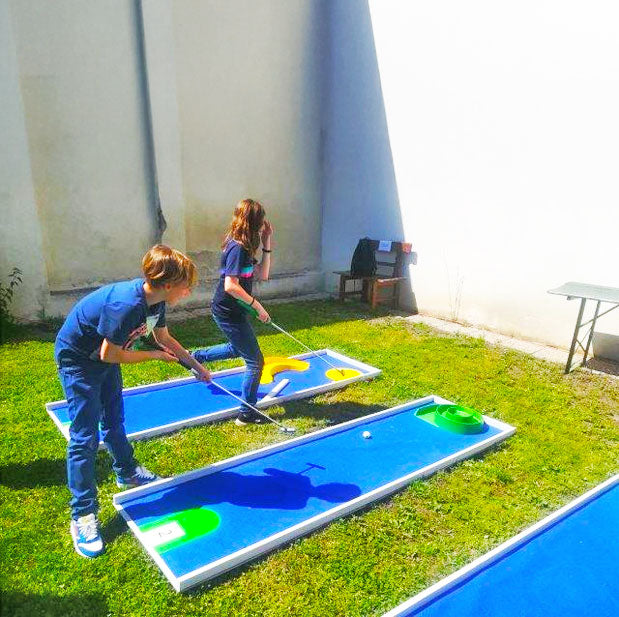 Zwei Kinder bei einer Mobilen Minigolfbahn mit verschiedenen Hindernissen auf einer gruenen Wiese