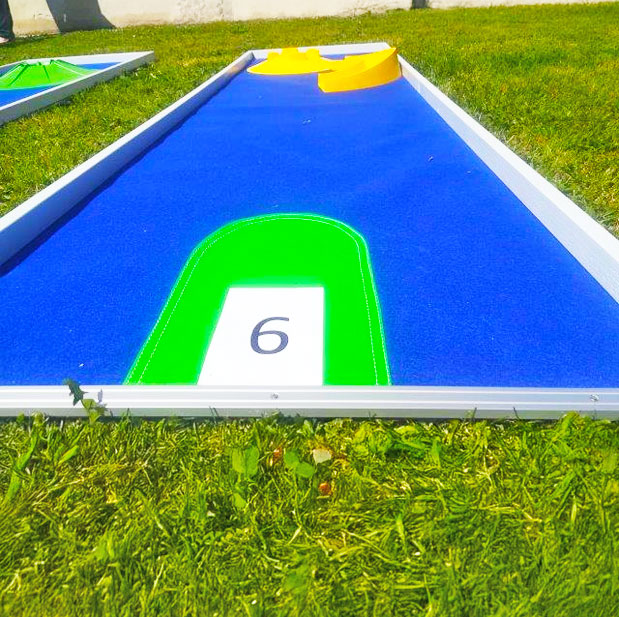 Eine Minigolfbahn in Blau mit einem gelben Hindernis auf einer gruenen Wiese