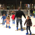 Zwei Erwachsene mit vielen Kindern auf einem Mobilen Eislaufplatz.