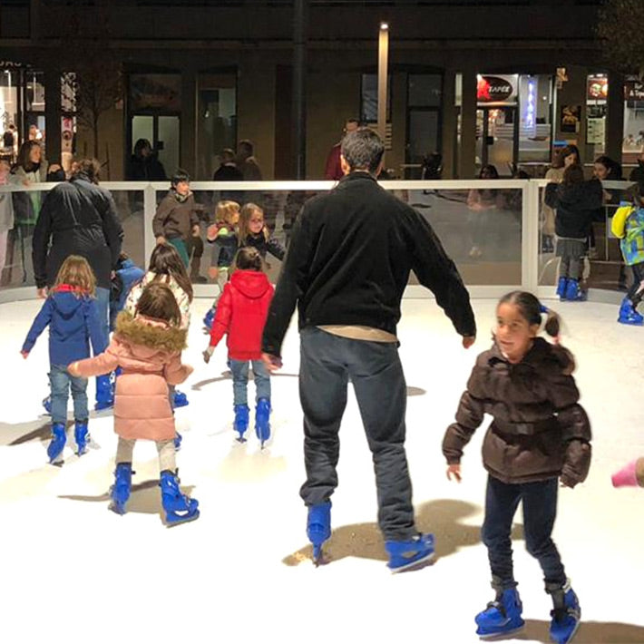 Zwei Erwachsene mit vielen Kindern auf einem Mobilen Eislaufplatz.