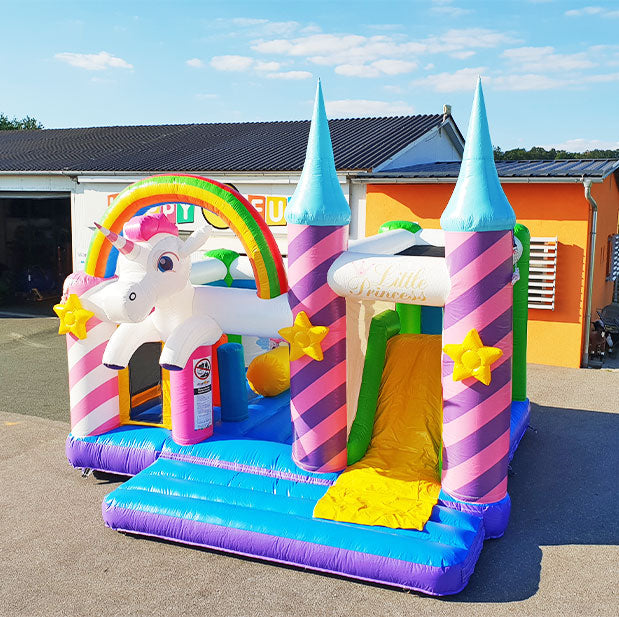 Aufblasbare Huepfburg mit einem riesigen Einhorn Kopf und darueber ein Regenbogen mit Sternen an den Saeulen und 2 Tuerme, eine Rutsche und Hindernisse