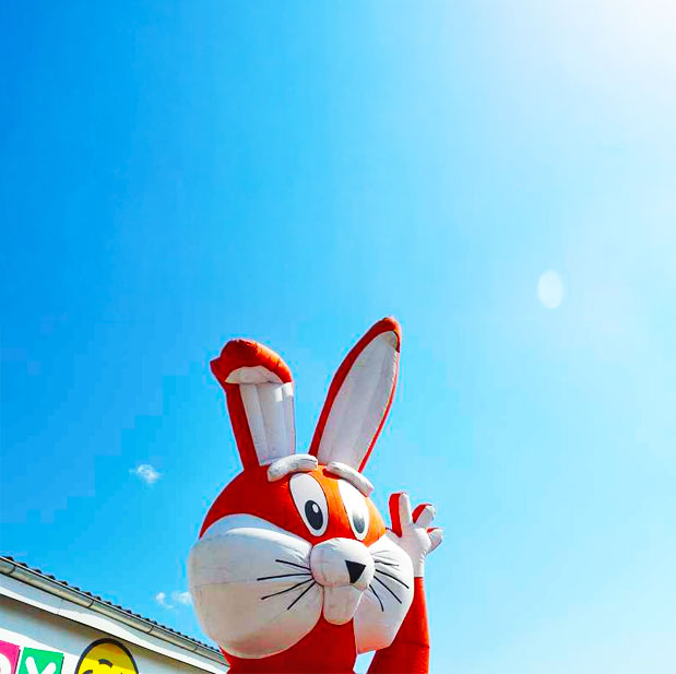 Aufblasbarer Hasenkopf mit einem abgeknickten und einem stehenden Ohr der die linke Hand hebt