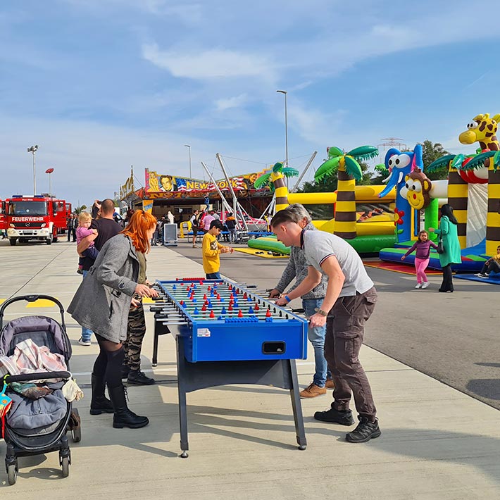 Vier Erwachsene die an einem Tischwuzzler auf einer Veranstaltung mit Spielgeraeten spielen.