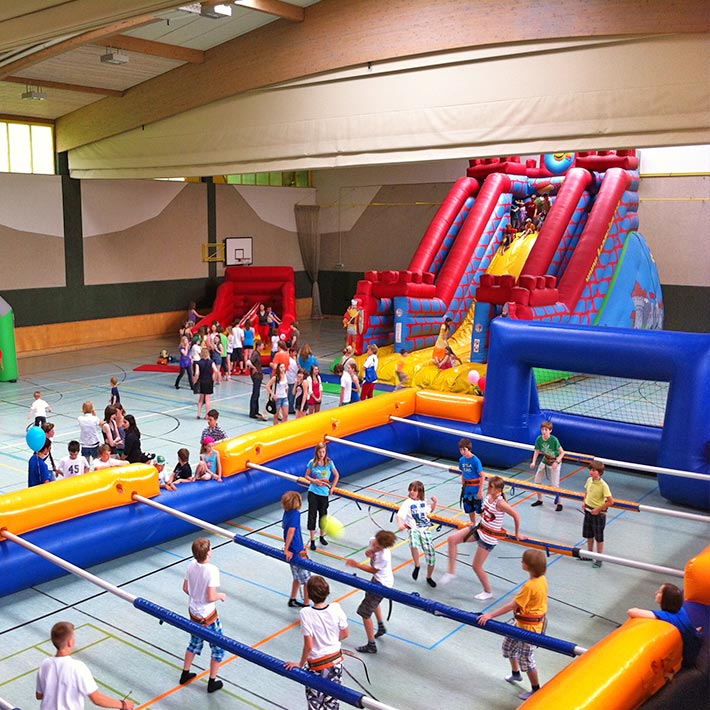 Kinder in einem Riesenwuzzler, der in einem Turnsaal neben einer Riesenrutsche aufgebaut ist.