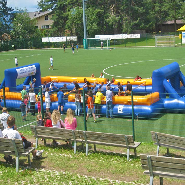 Riesenwuzzler mit mehrere Personen auf einem Fussballplatz mit Zuschauern.