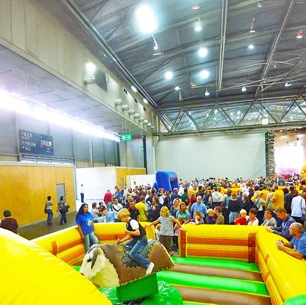 Ein Kind auf einem Rodeo mit einem Bullen der ein Fell hat in einer grossen Halle mit vielen Leuten