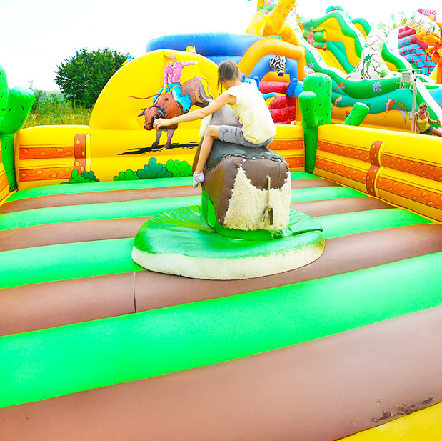 Ein Maedchen auf einem Rodeo mit einem aufblasbarem Fallbecken in Gruen-Braun gehalten