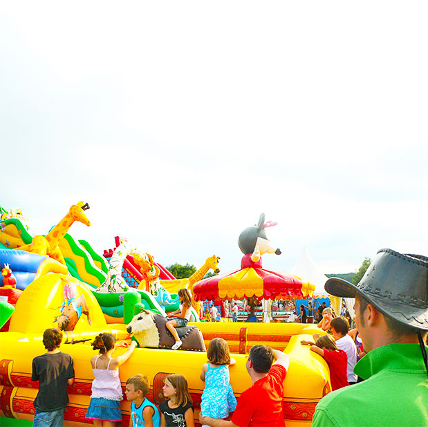 Aufblasbarer Rodeo mit einem Bullen auf dem ein Kind sitzt und Spass hat auf einem Fest mit vielen Besuchern