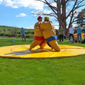 Maenner im gelben Sumo-Kostuem bei einem Sumo-Kampf auf einer gelben Matte.