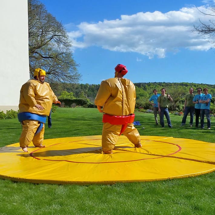 Zwei Personen in einem Sumo-Kostuem mit gelber Fallmatte zum mieten.
