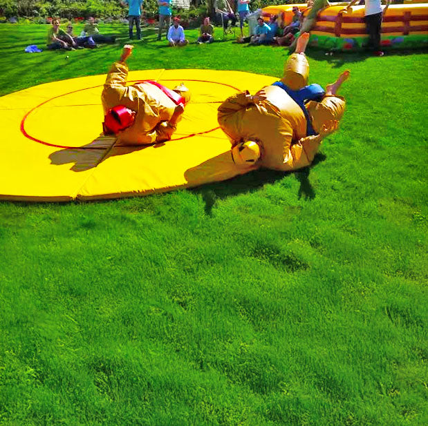 Zwei Personen bei einem Smo Kampf auf einer Gelben Matte die in der Wiese liegt und rundherum Zuschauer