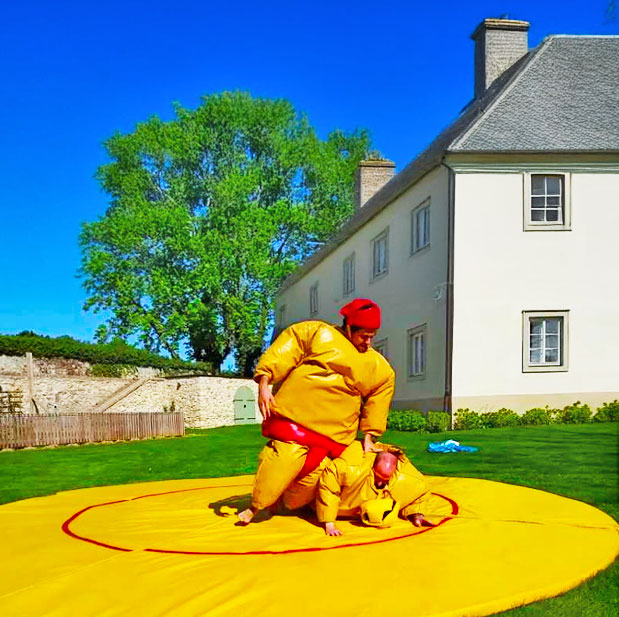 Ein Sumo Kaempfer liegt auf einem anderen Sumo Kaempfer auf einer Gelben Matte