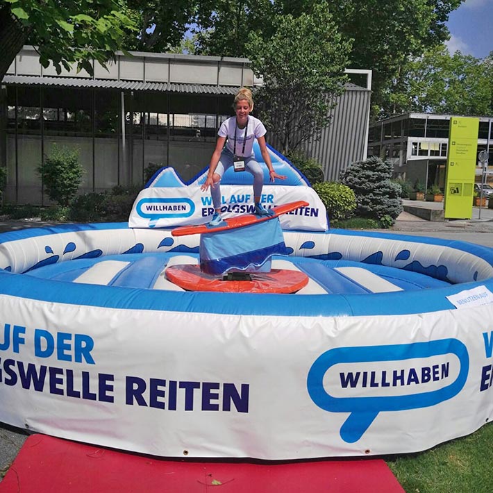 Eine Frau auf einem Surf-Simulator mit einem Fallbecken das gebrandet ist.