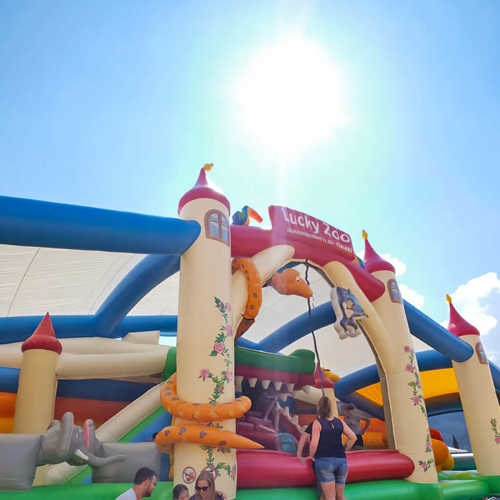 Bunte Hüpfburg im Schloss-Design mit riesigem Krokodil-Maul und detailreichen Tiermotiven - ein Blickfang für Abenteuer und Events.