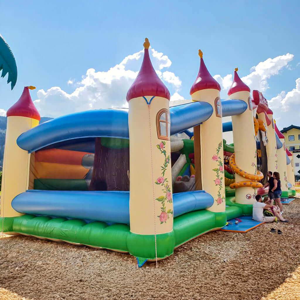 Riesige Hüpfburg im Märchenschloss-Design mit Türmen, Rutschen und Spielzonen - ein echtes Highlight für große Kinderveranstaltungen im Freien.
