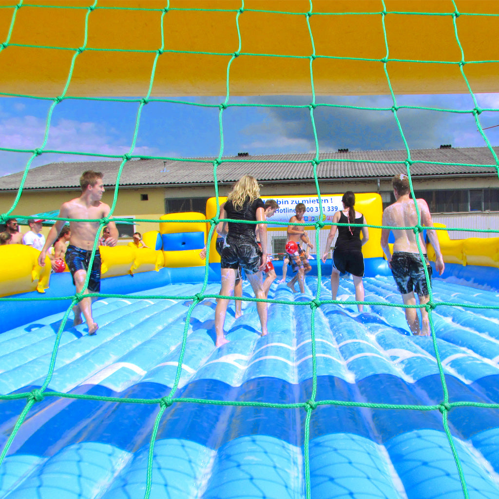 Kinder und Jugendliche spielen auf einer Hüpffläche, welche mit Wasser und Seife gefüllt ist, Fußball.