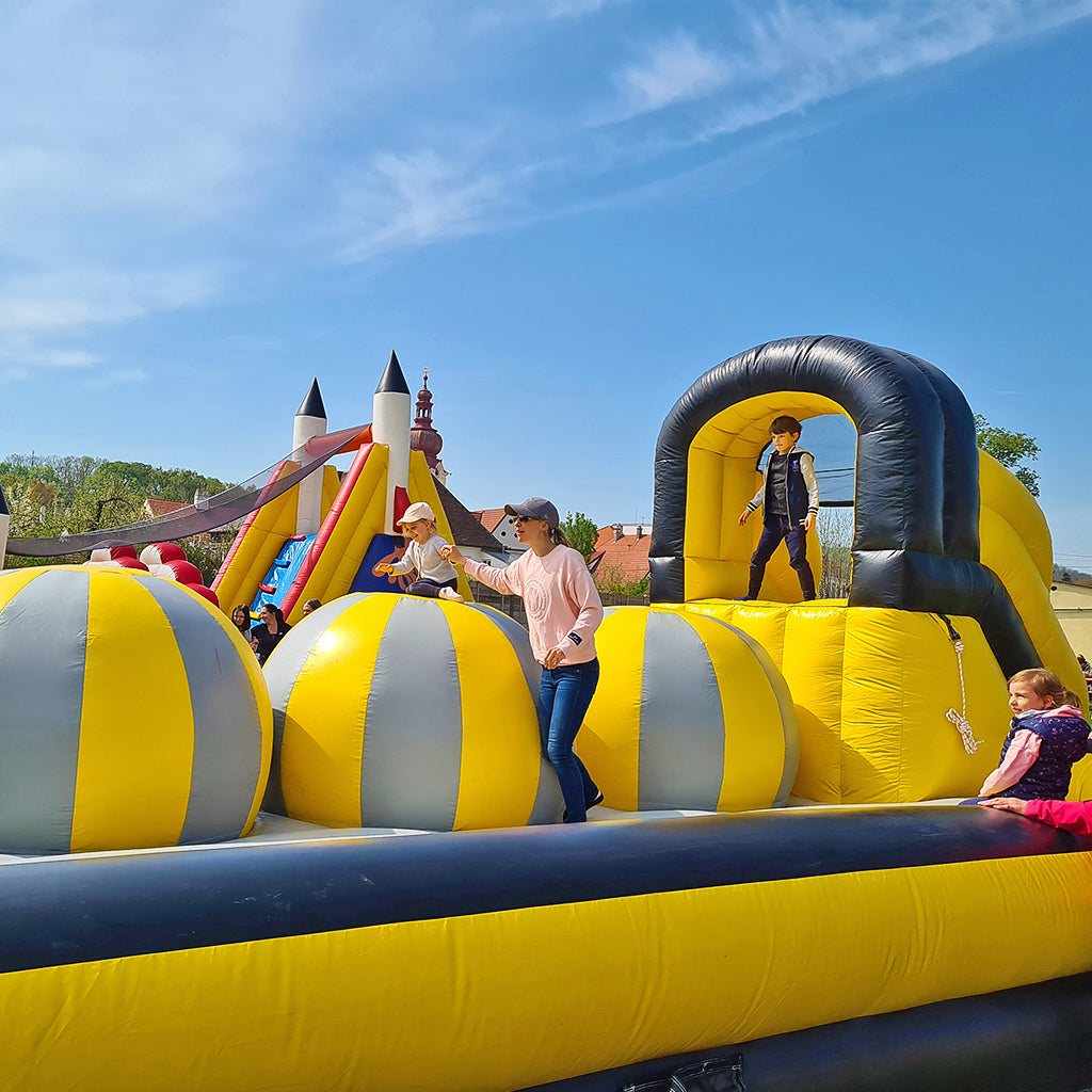 Schwarz-gelbe aufblasbare Hüpfburg mit großen Ballelementen als Hindernisse, für Kinder und Erwachsene.
