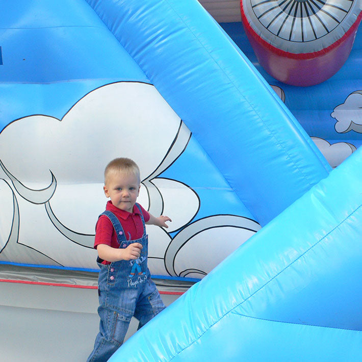 Kleiner Junge neben einer aufblasbaren Huepfburg.