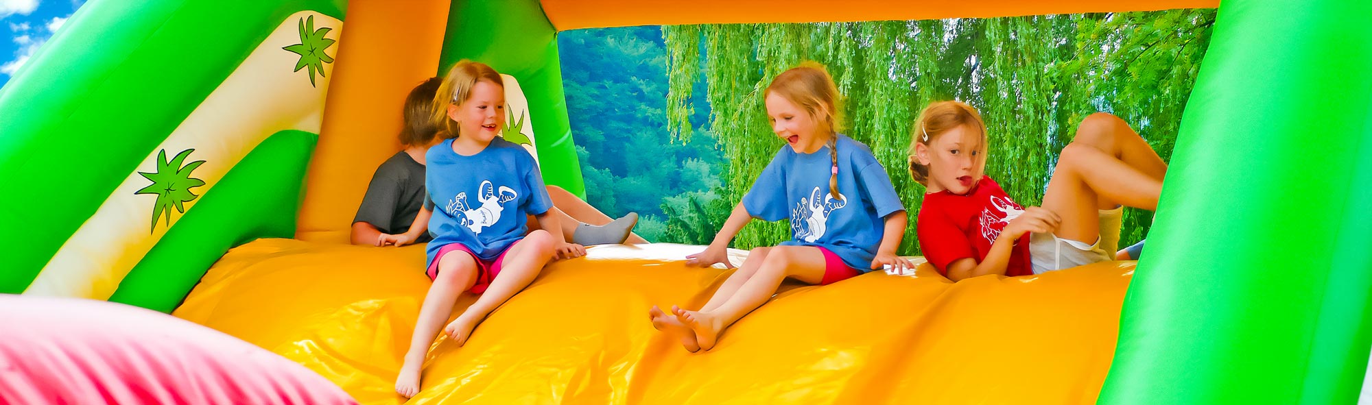 Fröhliche Kinder spielen lachend auf einer bunten happy Fun GmbH Hüpfburg im Freien