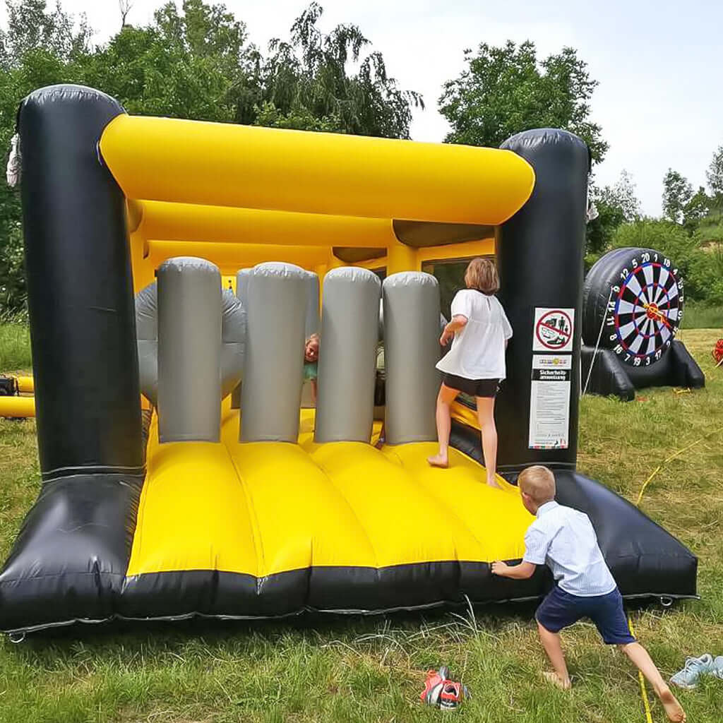 Ein Einstieg einer großen schwarz-gelben Hüpfburg, mit vier aufblasbaren ein und halb Meter Hohen Zylindern.