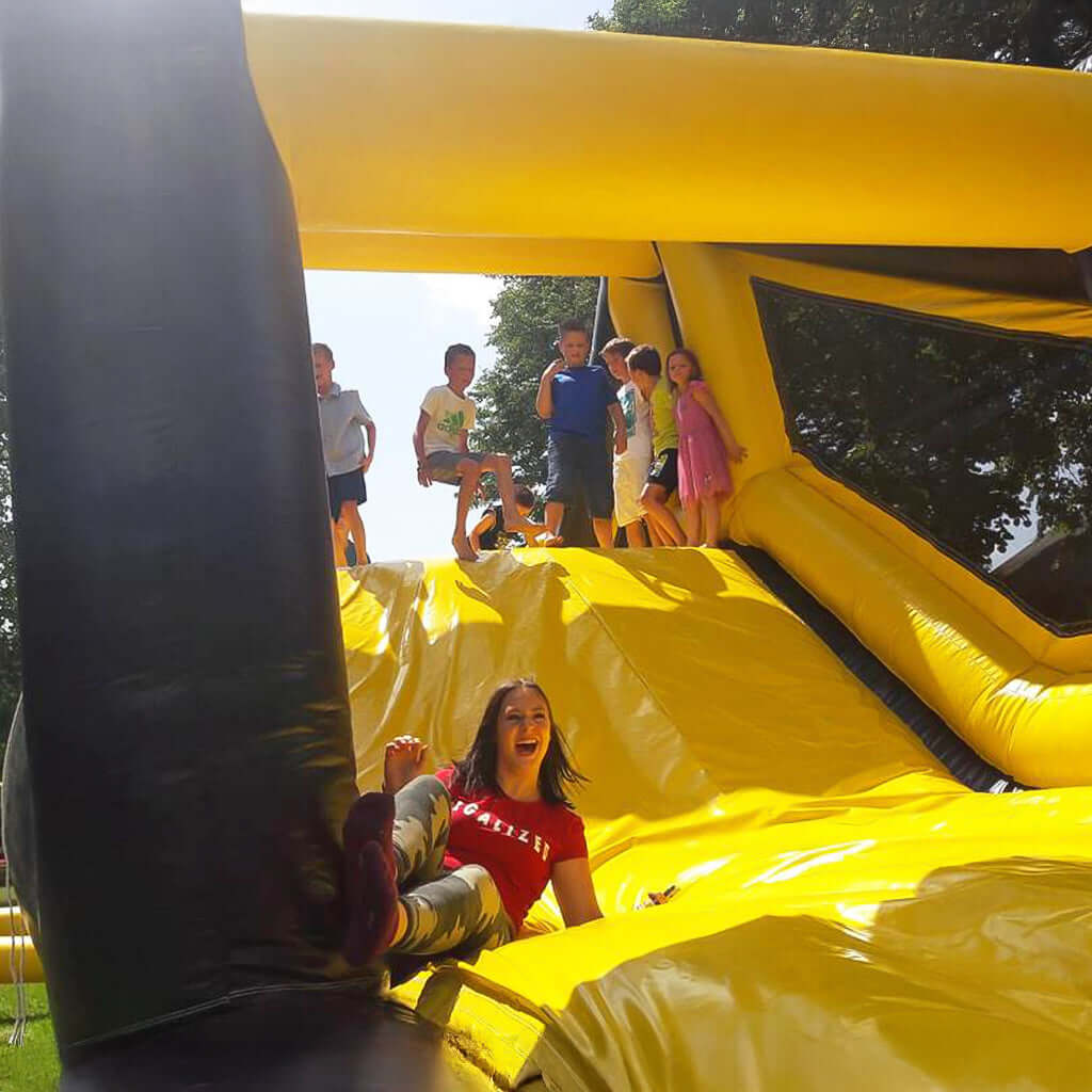 Ein gelbe Rutsche von einer Hüpfburg, mit vielen lachenden Kindern.