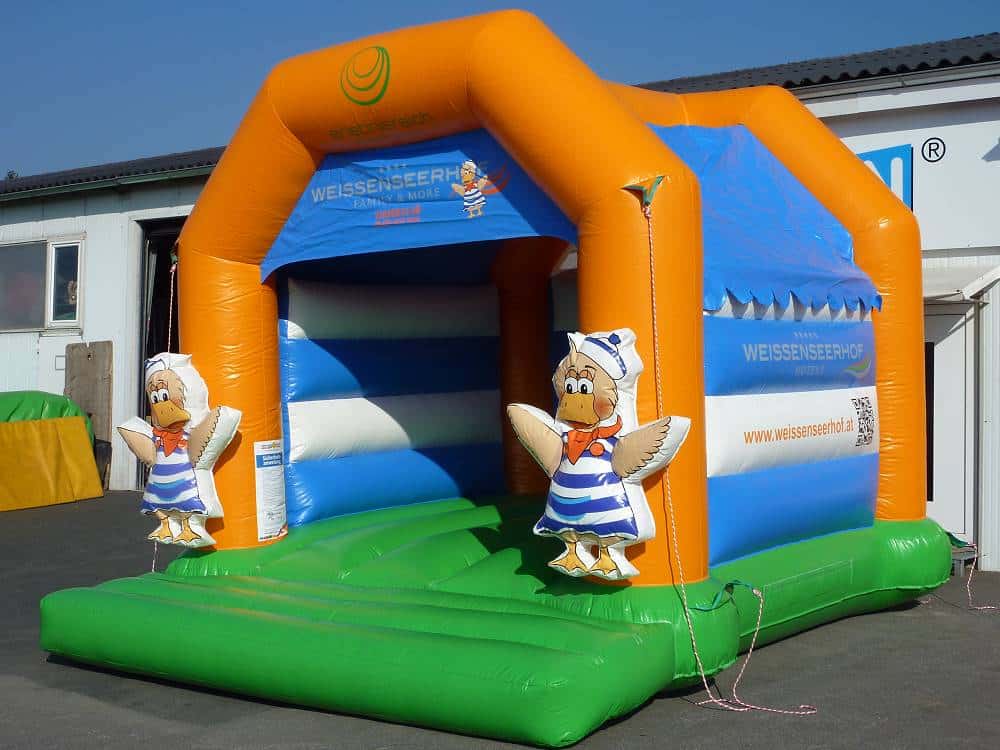 Hüpfburg auf einem Betonplatz vor einer Halle mit zwei Entenfiguren