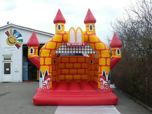 Farbenfrohe Hüpfburg von vorne mit vier Türmen und zwei Clowns an den Säulen