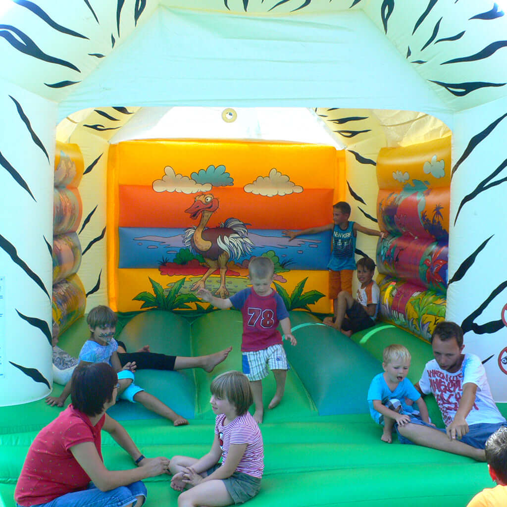 Grüne aufblasbare Hüpffläche mit vielen Kindern und einer schönen Rückwand Bemalung in Savannen Optik.