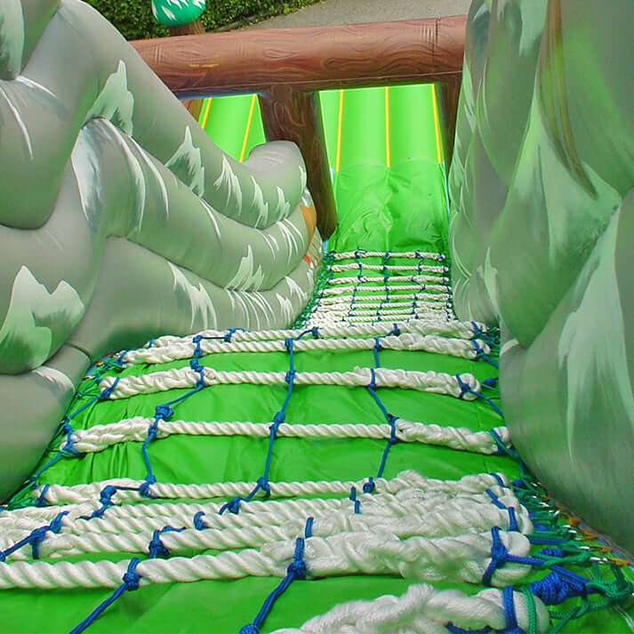 Aufblasbare Riesenrutsche mit Waldmotiv, Kletterbereich und zwei Rutschbahnen – detailreiche Gestaltung mit Bäumen und Holzoptik