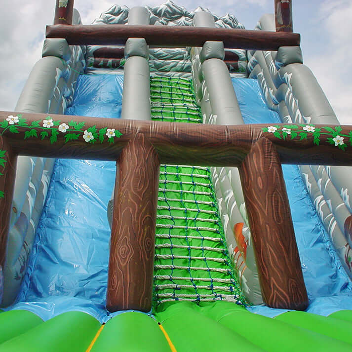 Aufblasbare Riesenrutsche mit Waldmotiv, Kletterbereich und zwei Rutschbahnen – detailreiche Gestaltung mit Bäumen und Holzoptik