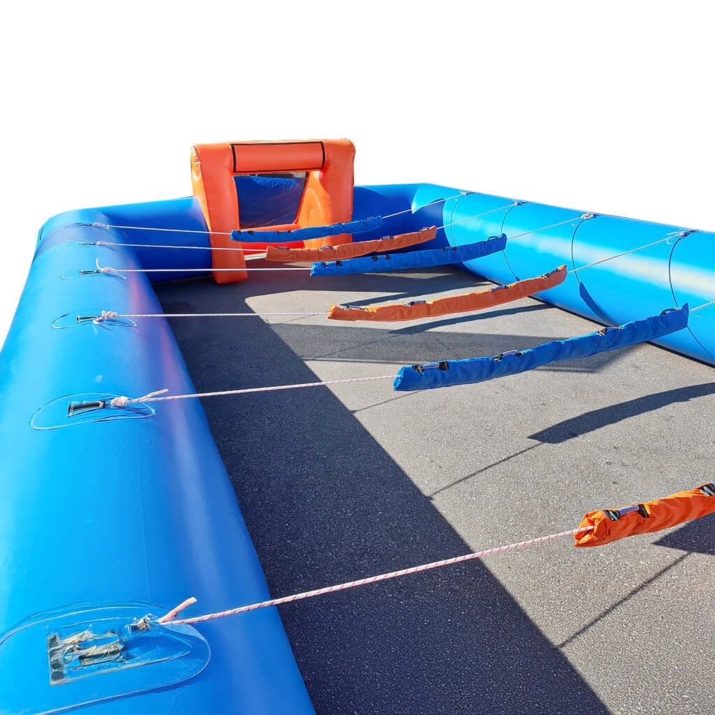 Menschenkicker mit blau-orangen Streben und aufblasbarem Tor, aufgebaut auf Asphaltfläche