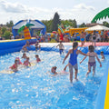 Ein großes aufblasbares Wasserbecken mit ganz vielen Kindern, welche schwimmen und plantschen.