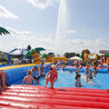 Aufblasbares Wasserbecken mit blauen Wänden gelben Palmen und vielen spielenden Kindern.