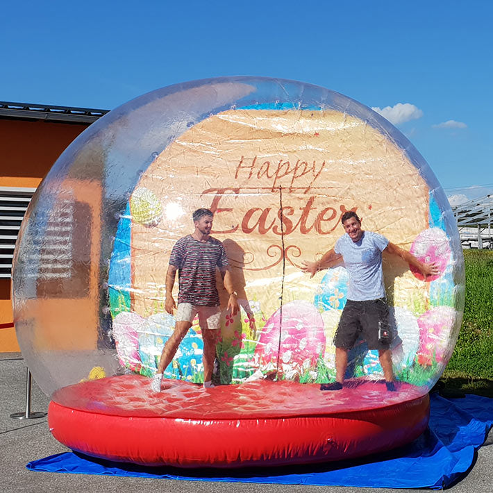 Zwei Maenner in einer aufblasbaren Fotokugel mit einem Bild für Ostern im Hintergrund.