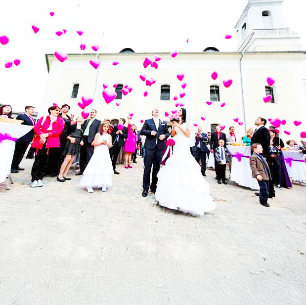 Froehliche Mensche die eine Hochzeit feiern und Herzluftballone steigen lassen 