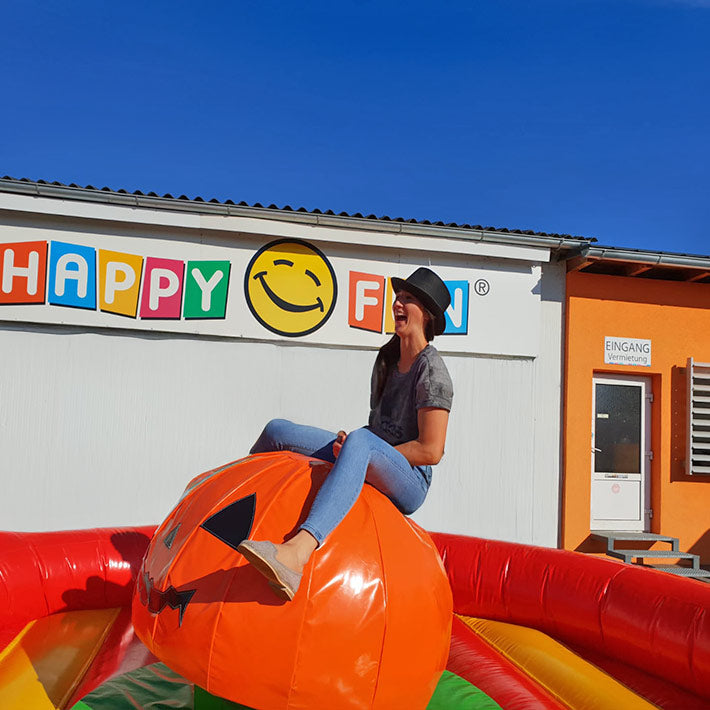 Lachende Frau mit Hut auf einem Kuerbis Rodeo vor einer Halle im freien.