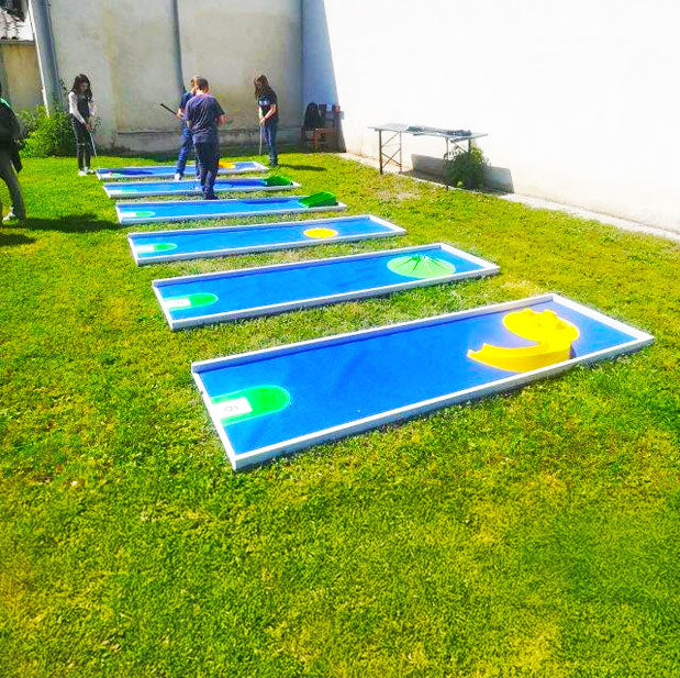 Froehliche Kinder die an einer blauen Mobilen Minigolfbahn spielen die auf einer Wiese aufgelegt ist.