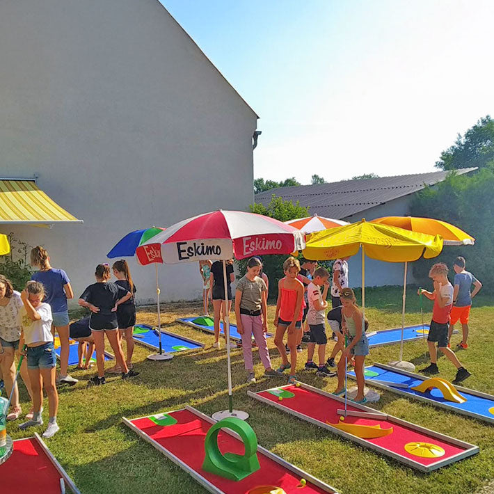 Mobile Minigolf Anlage zu mieten mit vielen Kindern die unter Sonnenschirmen stehen.